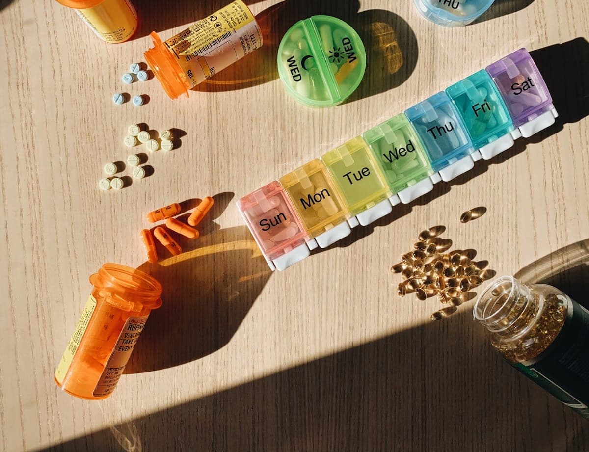Amber prescription bottles and a rainbow weekly pill organizer with English day labels on a warm wood surface